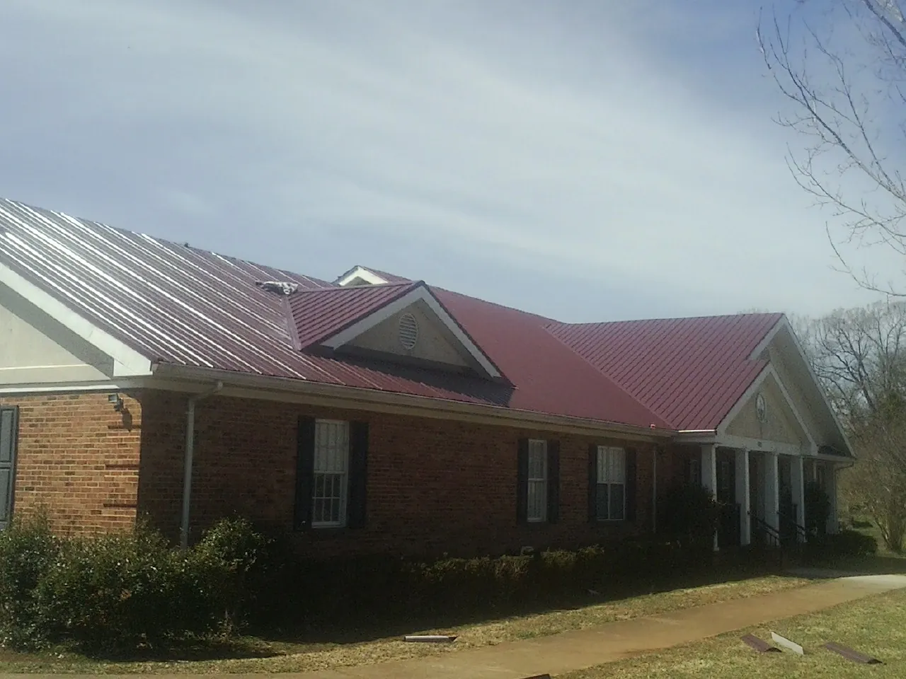 Red metal roof with gabled entries on a long brick building, from a Hail Damage Roof Repair job in Sagamore Beach