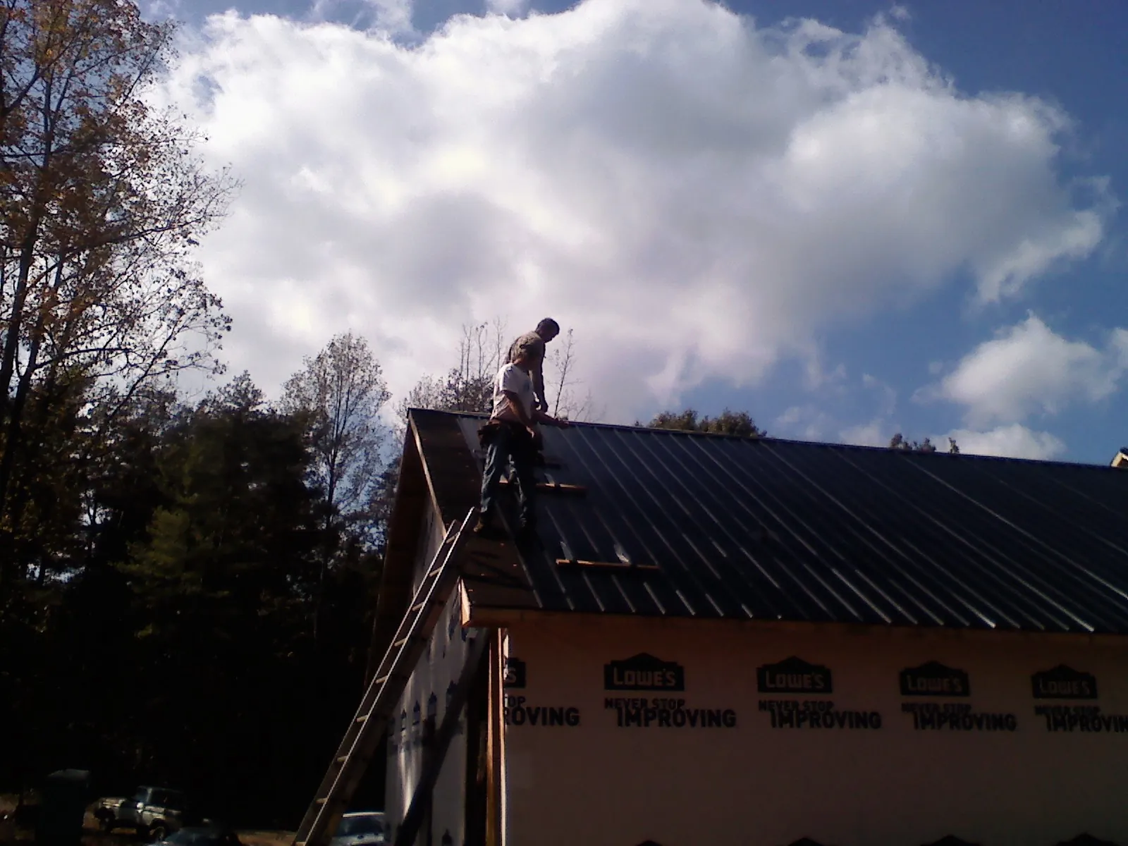 Roofer fastening dark metal panels high against a cloudy sky, from a Roof Inspection job in Sagamore Beach