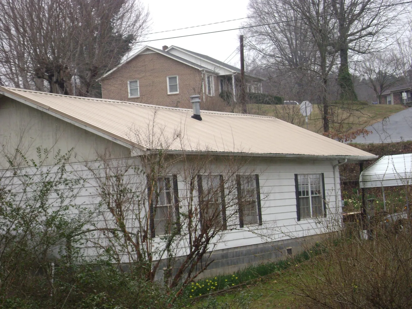 Tan metal roof on a white sided house set into a hillside — Commercial Roofing by Roofing Brothers in Sagamore Beach