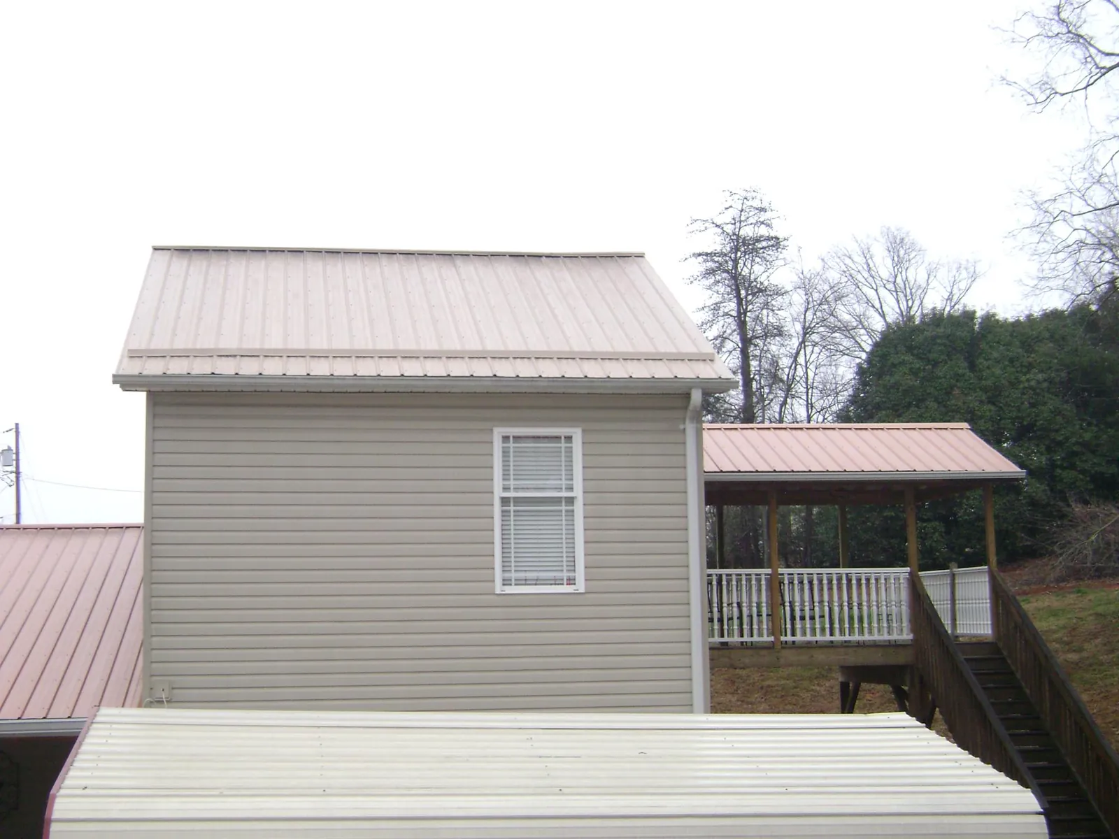 Tan metal roofs on a two story addition and attached porch, from a Roof Replacement job in Sagamore Beach