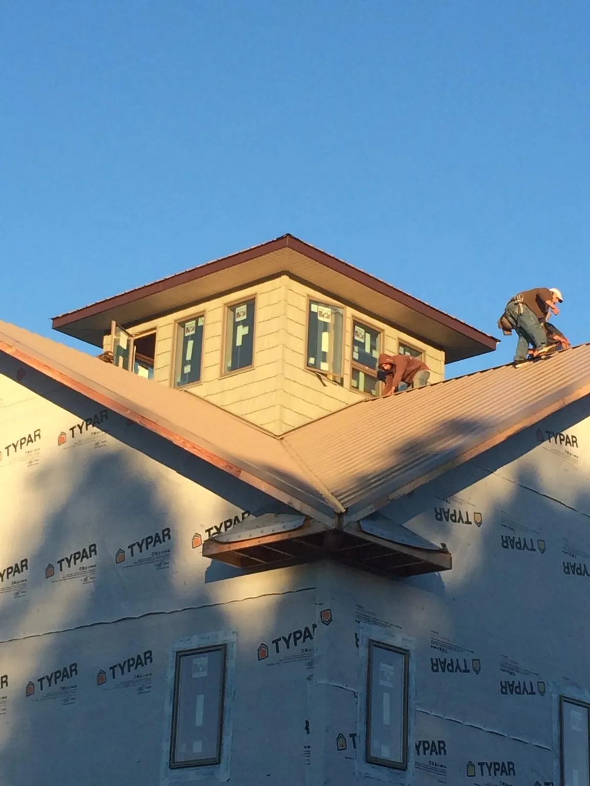 Roofers working around a rooftop cupola on a new metal roof at sunset — Roof Waterproofing in Sagamore Beach by Roofing Brothers